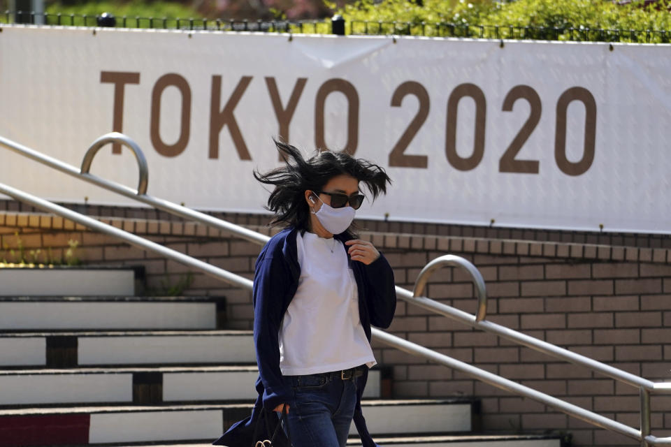 A woman wearing a protective mask to help curb the spread of the coronavirus walks near a banner for Tokyo 2020 Olympic and Paralympic Games Wednesday, March 31, 2021, in Tokyo. The Japanese capital confirmed more than 410 new coronavirus cases on Wednesday. (AP Photo/Eugene Hoshiko)