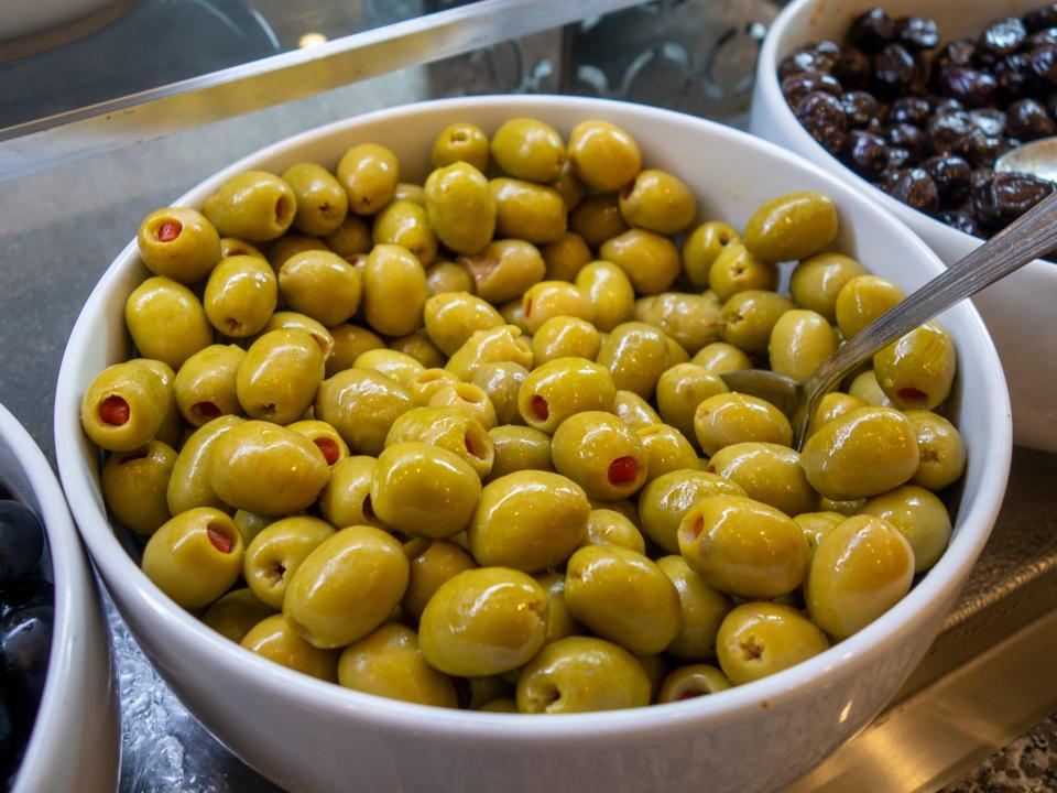 bowls of green and black olives and similar produce at a grocery store