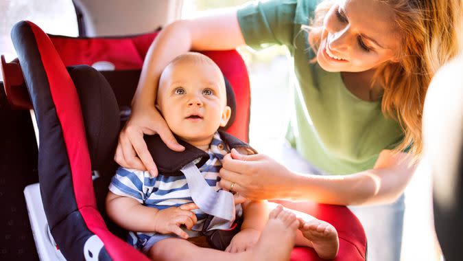 Young mother putting her little baby boy in the car seat, fastening seat belts.