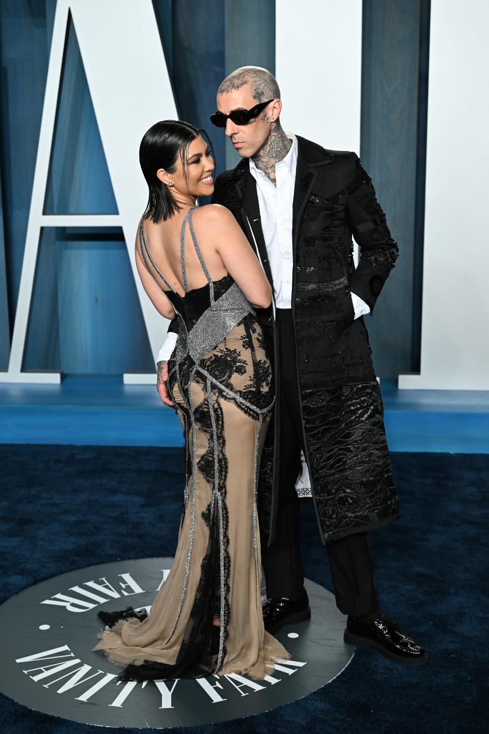 Kourtney in a beige, black, and silver gown with lace, cutouts, and straps.