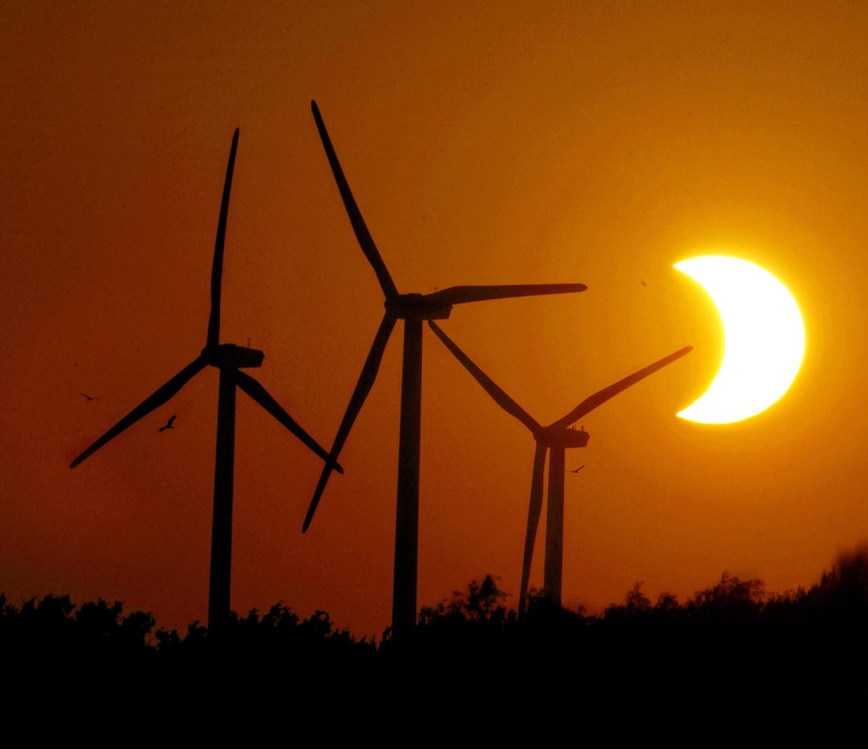 Hawks and wind turbines spin lazy circles in the air near Trent, Texas, as a partial eclipse of the sun makes for a unique sunset June 10, 2002.