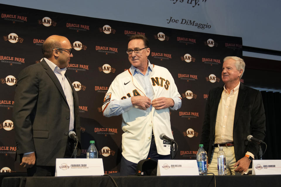 San Francisco Giants new manager Bob Melvin puts on his new jersey as President of Baseball Operations Farhan Zaidi, left, and Chairman Greg Johnson, right, look on during an introductory baseball news conference at Oracle Park in San Francisco, Wednesday, Oct. 25, 2023. (AP Photo/Eric Risberg)