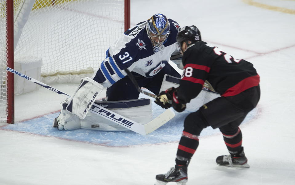 Winnipeg Jets goaltender Connor Hellebuyck, left, makes a save against Ottawa Senators right wing Connor Brown during second-period NHL hockey game action Monday, April 12, 2021, in Ottawa, Ontario. (Adrian Wyld/The Canadian Press via AP)