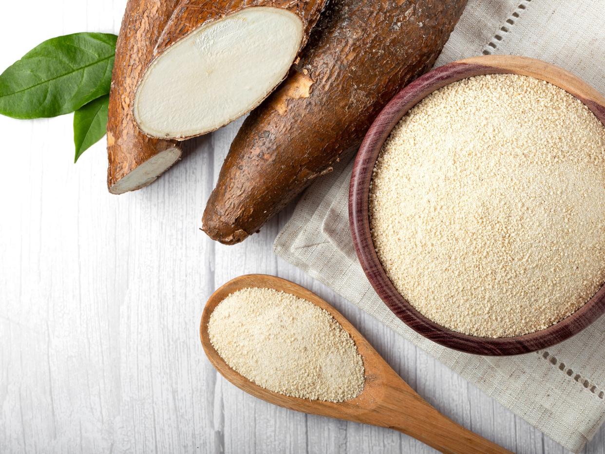 Cassava root and flour in a wooden bowl with wooden spoon