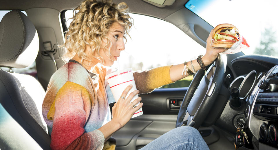 A woman eating burgers from a fast food chain while driving a car. Source: Getty Images