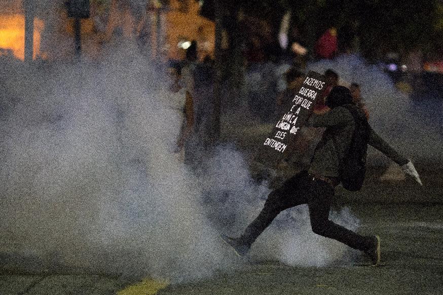 Holding a shield covered with the Portuguese message: "We make war because is the only language they understand," a demonstrator runs amid tear gas during a demonstration against federal government proposed reforms in Rio de Janeiro, Brazil, Wednesday, March 15, 2017. People protested across the country against proposed changes to work rules and pensions. (AP Photo/Leo Correa)