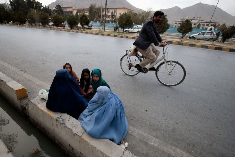 FILE PHOTO: Women wearing burqas sit with their children as the beg along a road in Kabul