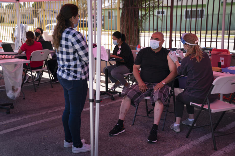 Accompanied by wife, Mariana Jimenez, left, Weldin Lemus, center, receives the Johnson & Johnson's COVID-19 vaccine from registered nurse Anne-Marie Zamora at a Cedars-Sinai sponsored pop-up vaccine clinic at the Watts-Willowbrook Boys & Girls Club in Los Angeles, Wednesday, April 28, 2021. California, swimming in vaccine, is in a far different place than it was just weeks ago when simply scoring an appointment was cause for celebration. Today, Los Angeles, San Diego and other populous counties are advertising that anyone can walk in for a shot and the state is texting reminders that plenty of appointments are available. (AP Photo/Jae C. Hong)