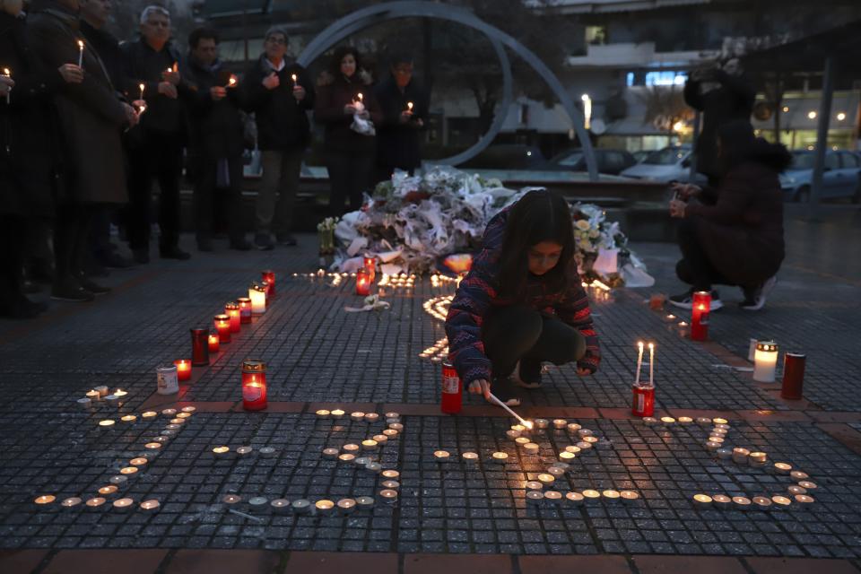 A girl lights a candle, in memory of the trains collision victims, outside the train station of Larissa city, about 355 kilometres (222 miles) north of Athens, Greece, Thursday, March 2, 2023. Emergency crews inched through the mangled remains of passenger carriages in their search for the dead from Tuesday night's head-on collision, which has left dozens passengers dead in Greece's worst recorded rail accident. (AP Photo/Vaggelis Kousioras)