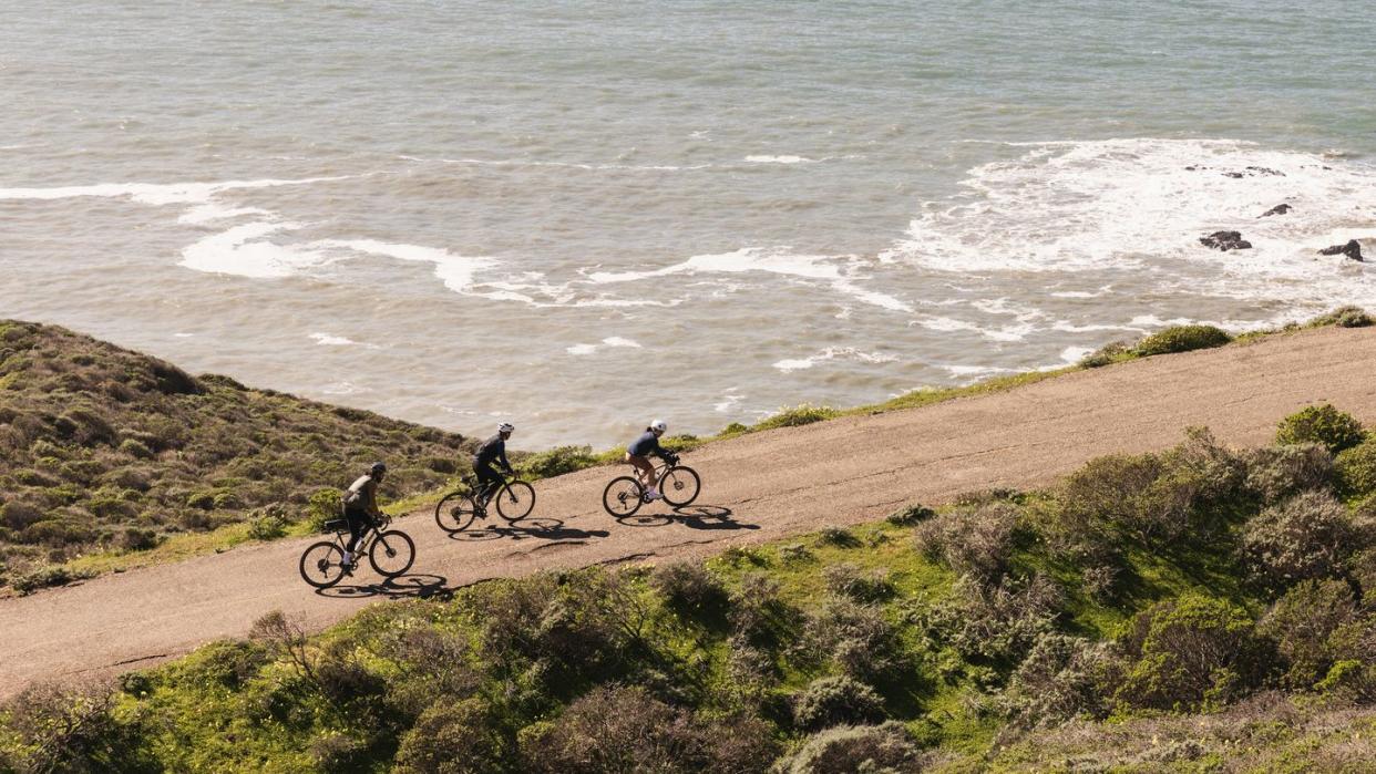 a group of people riding bikes on a road by the ocean