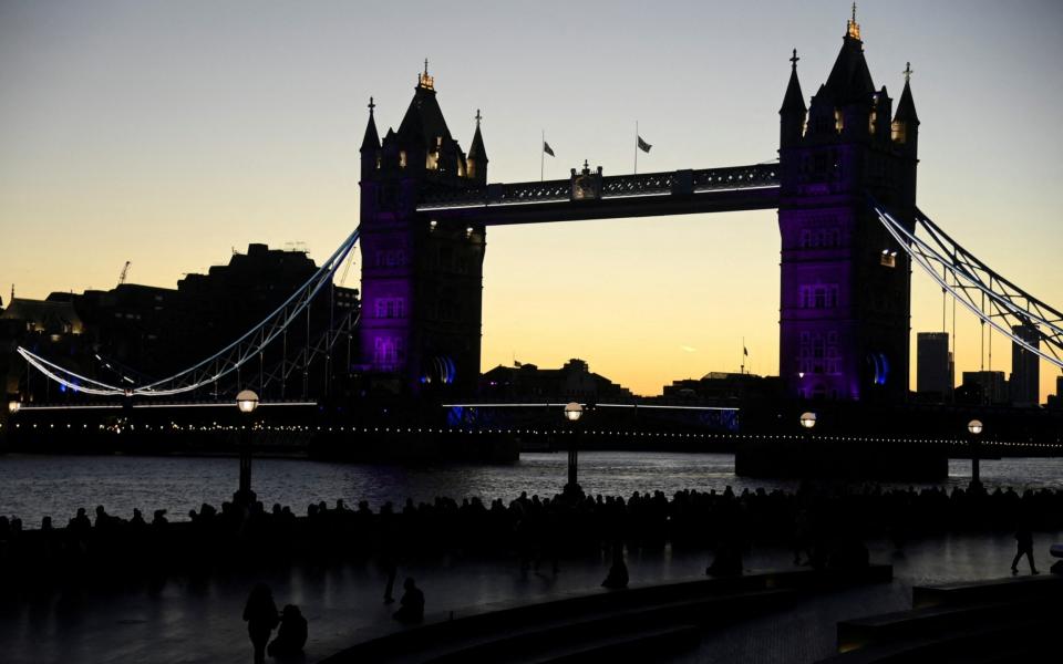 People are seen silhouetted as they queue before sunrise to pay their respects, as the Tower Bridge is lit up in purple to honour Britain's Queen Elizabeth, following her death, in London, Britain, September 17, 2022 - TOBY MELVILLE