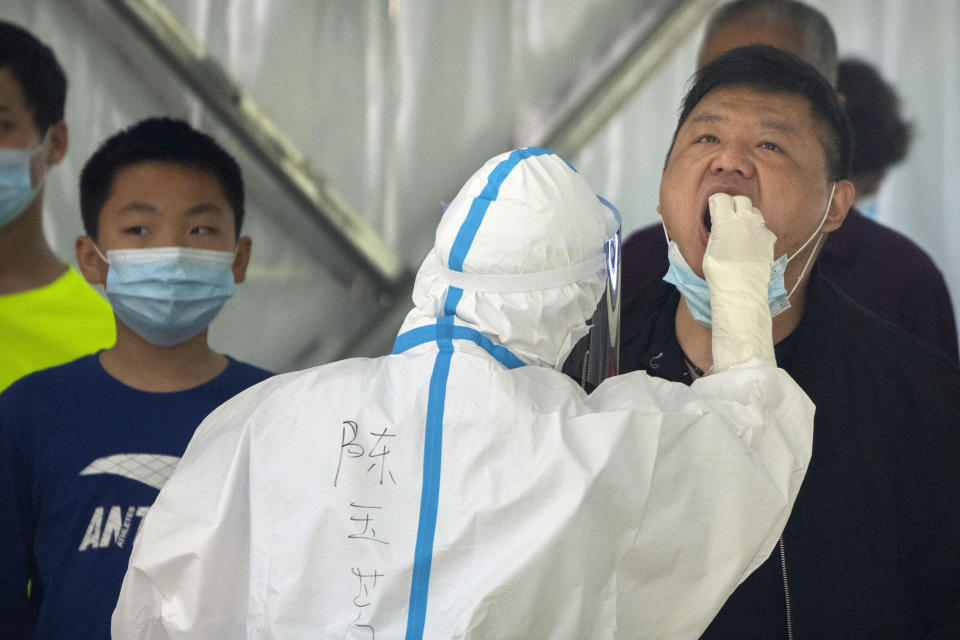 A worker wearing a protective suit swabs a man's throat for a COVID-19 test at a testing site during the second consecutive day of mass testing in Beijing, Wednesday, May 4, 2022. Beijing on Wednesday closed around 10% of the stations in its vast subway system as an additional measure against the spread of coronavirus. (AP Photo/Mark Schiefelbein)