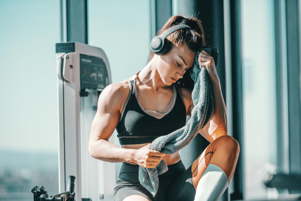 Serious muscular strong female bodybuilder with ponytail and headphones wiping sweat while sitting in gym next to window. The start is what stops most people.