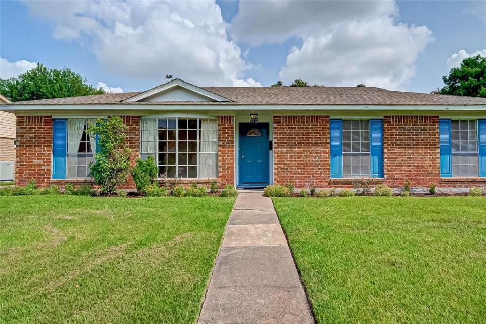 The exterior of the house for sale in Houston with a lawn out front and a blue door