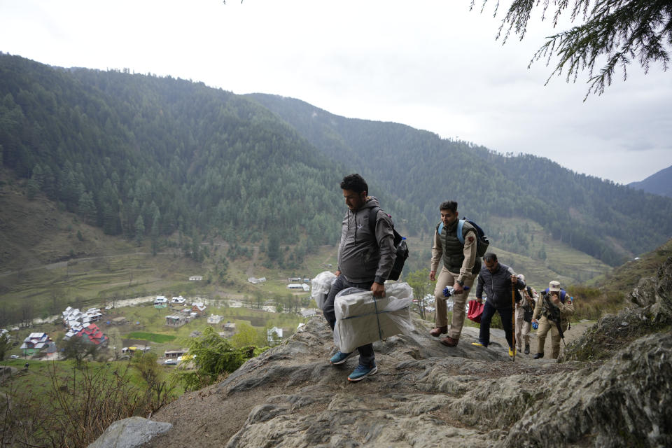 A man carries electronic voting machines as election officials walk to a polling booth in a remote mountain area on the eve of the first round of voting in the six-week long national election at Dessa village in Doda district, Jammu and Kashmir, India, April 18, 2024. (AP Photo/Channi Anand)