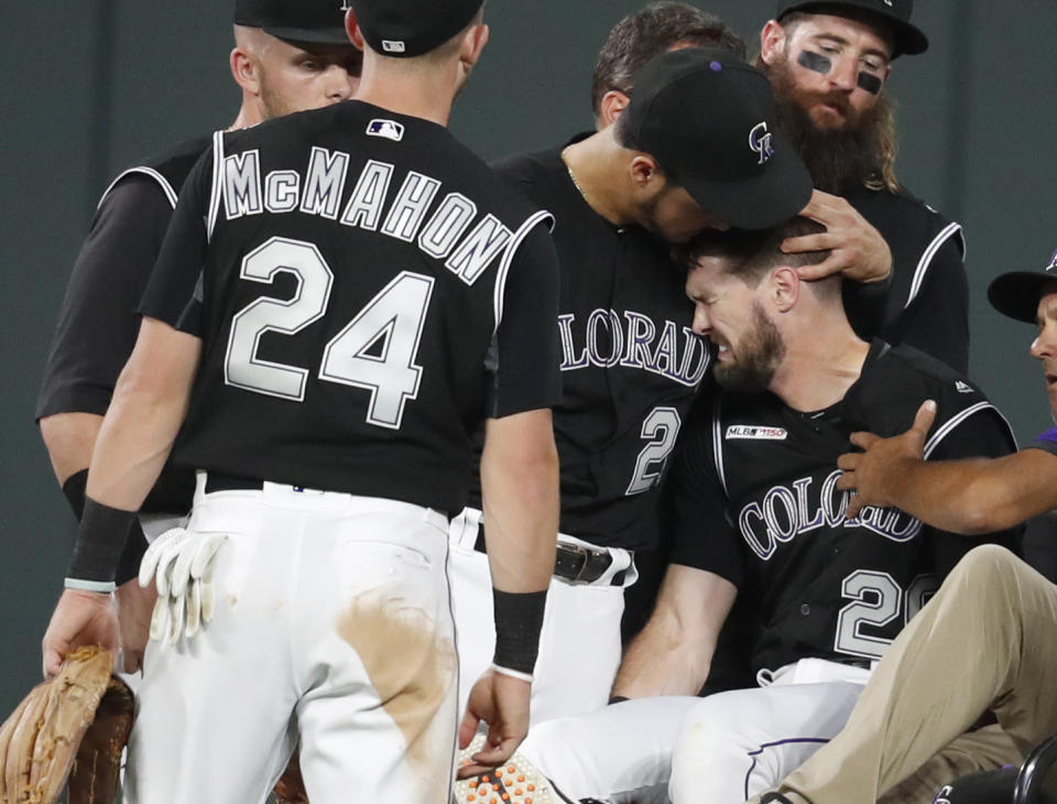 Colorado Rockies third baseman Nolan Arenado, left, consoles center fielder David Dahl, who suffered and injury to his right leg while catching a fly ball hit by San Francisco Giants' Scooter Gennett during the sixth inning of a baseball game Friday, Aug. 2, 2019, in Denver. (AP Photo/David Zalubowski)