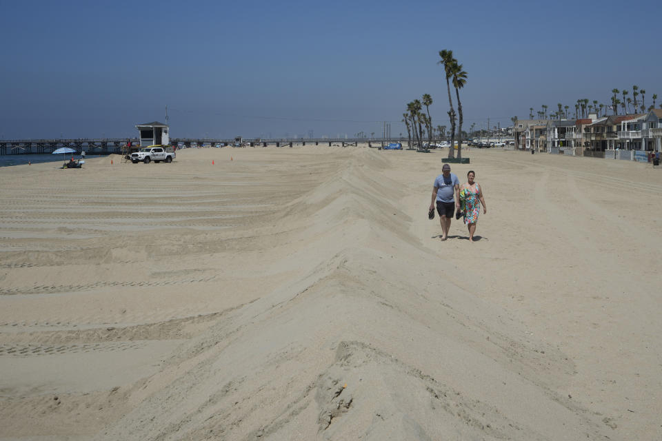 A couple walks along berms in Seal Beach, Calif., Friday, Aug. 18, 2023. Officials in Southern California were also re-enforcing sand berms, built to protect low-lying coastal communities against winter surf. Hurricane Hilary is churning off Mexico's Pacific coast as a powerful Category 4 storm threatening to unleash torrential rains on the mudslide-prone border city of Tijuana before heading into Southern California as the first tropical storm there in 84 years. (AP Photo/Damian Dovarganes)