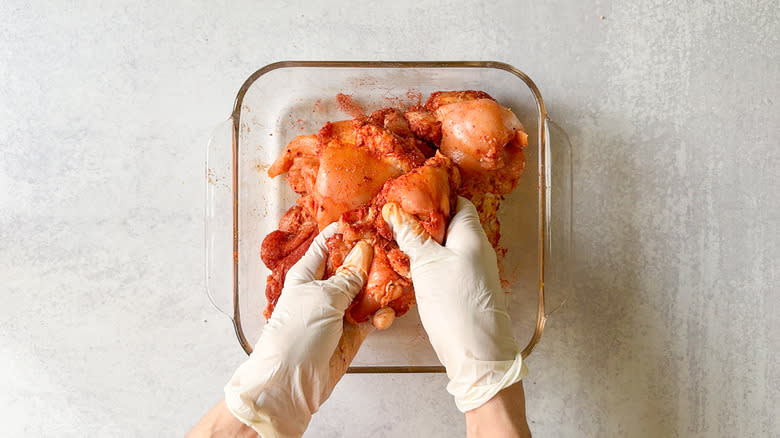 Rubbing spices into chicken thighs with gloves in glass baking dish