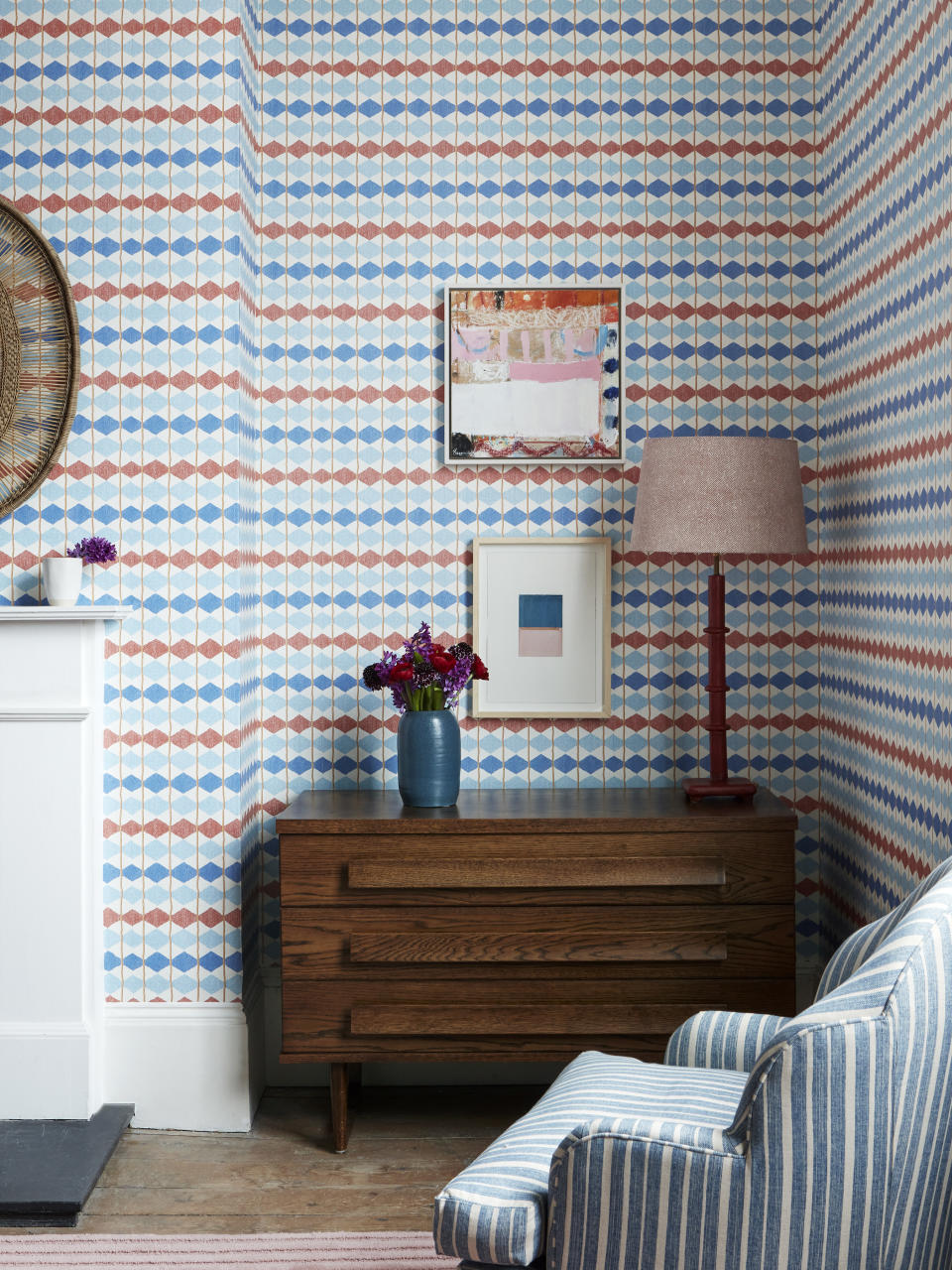 living room with geo stripe wallpaper in blues and red, stripe blue armchair,  retro chest of drawers, artwork, lamp