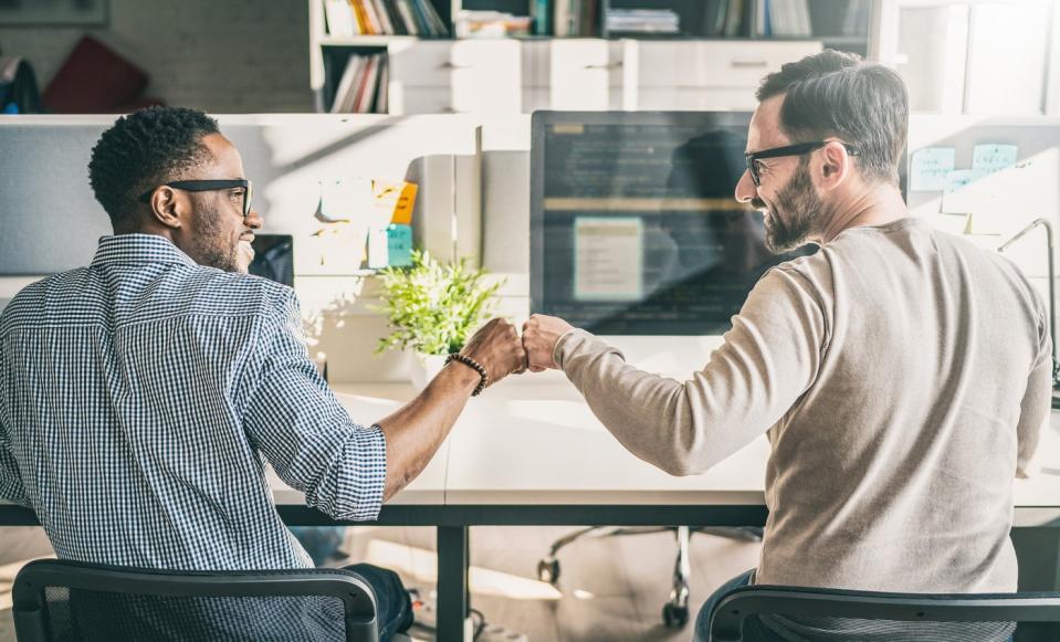 Two business partners sitting at desk celebrating success with a fist bump