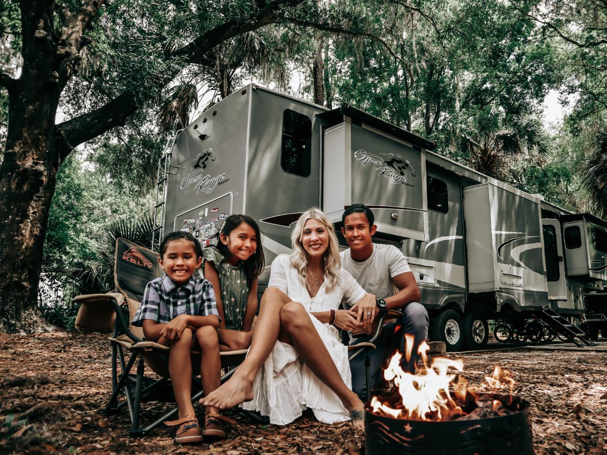 Family of four by campfire with large RV home in the background