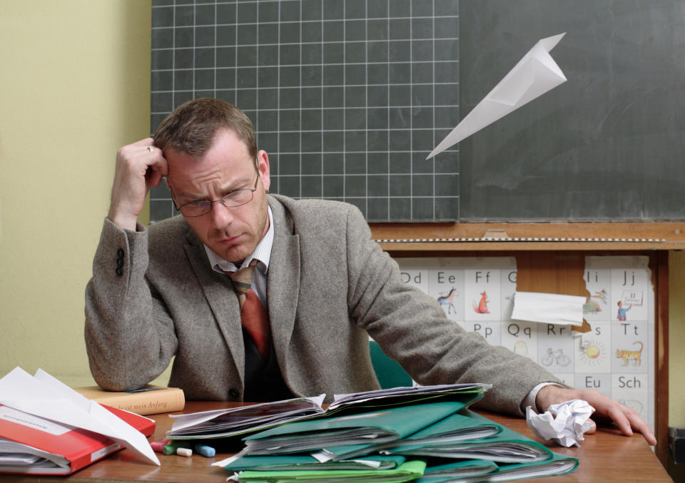 A teacher at his desk with a bunch of folders in front of him