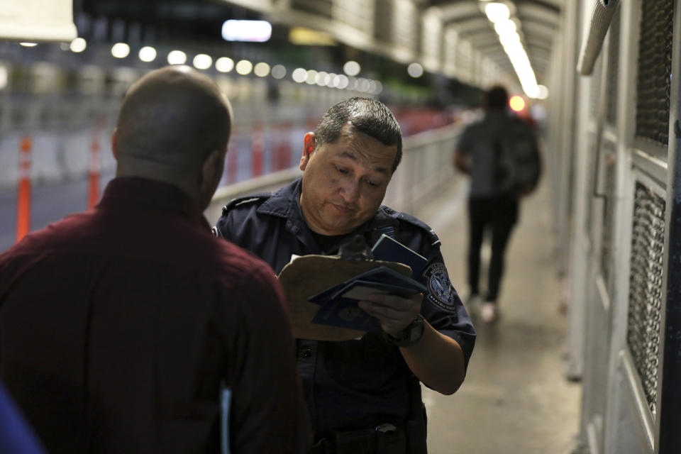 A U.S. Customs and Border Protection officer checks the documents of migrants who are on their way to apply for asylum in the United States, on International Bridge 1 as they depart Nuevo Laredo, Mexico, early Tuesday, Sept. 17, 2019. Tent courtrooms opened Monday in two Texas border cities to help process thousands of migrants who are being forced by the Trump administration to wait in Mexico while their requests for asylum wind through clogged immigration courts. (AP Photo/Fernando Llano)