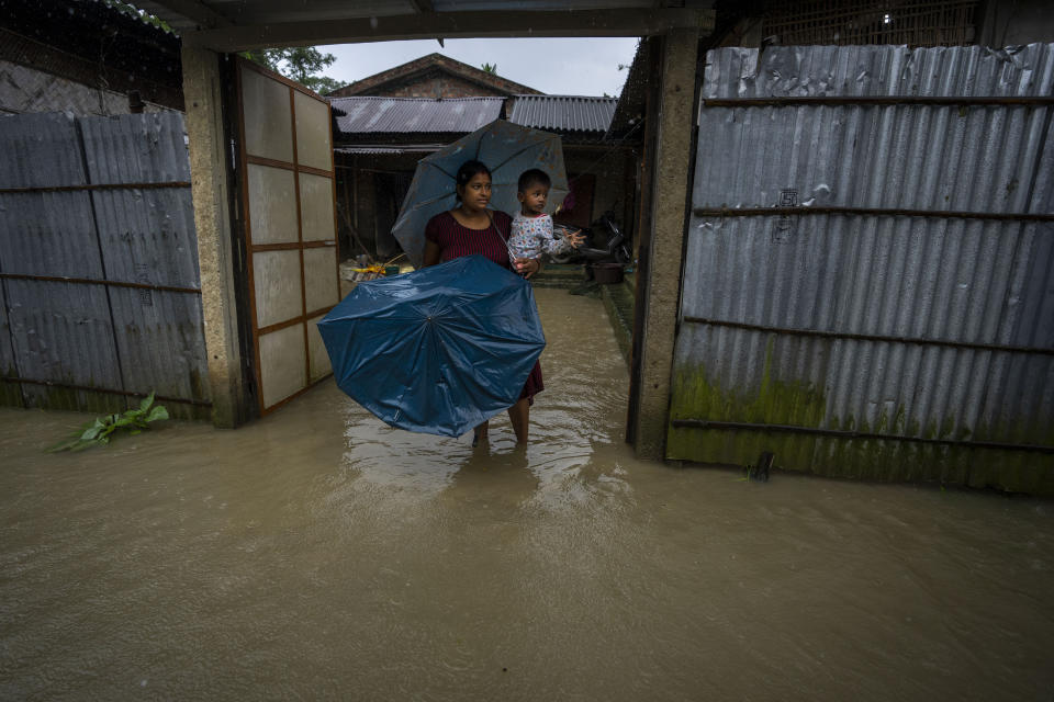 A woman holds a child and stands in floodwaters watching Indian army soldiers rescue flood-affected villagers on a boat in Jalimura village, west of Gauhati, India, Saturday, June 18, 2022. More than a dozen people have died as massive floods ravaged northeastern India and Bangladesh, leaving millions of homes underwater and severing transport links, authorities said Saturday. (AP Photo/Anupam Nath)