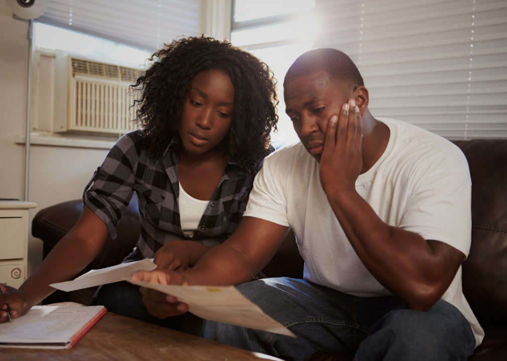 A worried African American couple is looking at papers in front of them. 