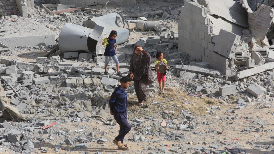 Adults and children in Rafah, walking through an area of concrete rubble after an attack by Israel