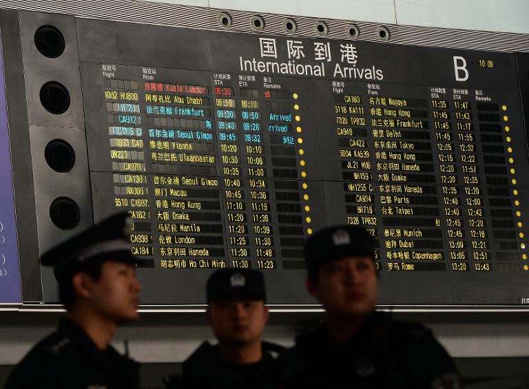 Chinese police stand beside the arrival board showing the flight MH370 (top-red) at the Beijing Airport after news of the Malaysia Airlines Boeing 777-200 plane disapeared on March 8, 2014