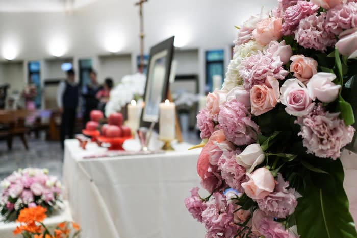 A funeral service, with a table with a picture of the diseased surrounded by candles, and flowers in the foreground.