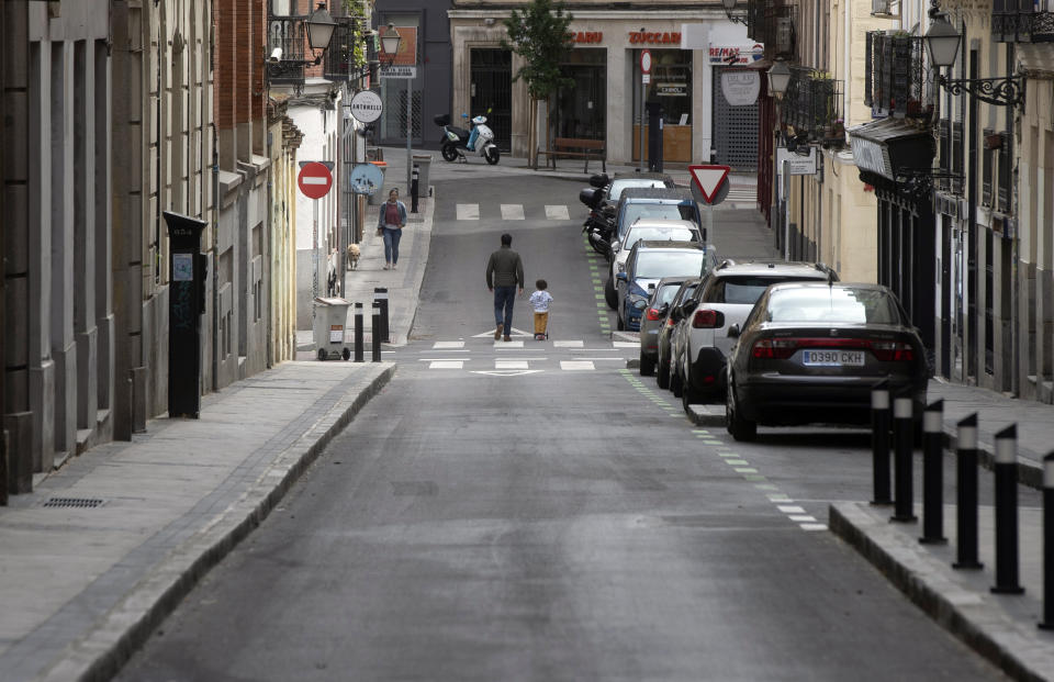 A man takes a young boy for a walk in Madrid, Spain, Sunday, April 26, 2020. On Sunday, children under 14 years old are allowed to take walks with a parent for up to one hour and within one kilometer from home, ending six weeks of compete seclusion due to the coronavirus outbreak. (AP Photo/Paul White)