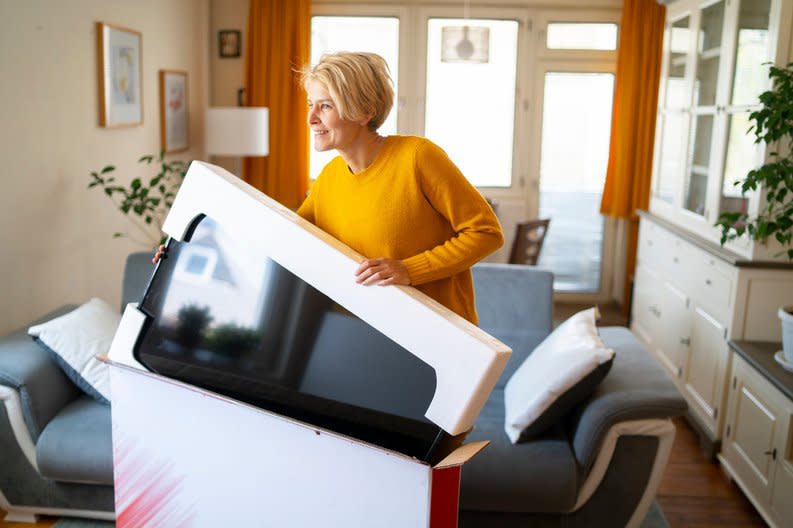 A person takes a new television out of the box in their living room.