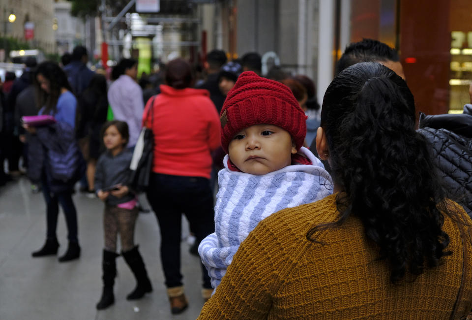 A woman holds a child in a line snaking around the block outside a U.S. immigration office with numerous courtrooms Thursday, Jan. 31, 2019, in San Francisco. The crowd was mixed with people who had court appointments for Thursday, people whose appointments were swallowed up by shutdown and others who had 'Notices to Appear' but assumed that meant they had court dates. (AP Photo/Eric Risberg)