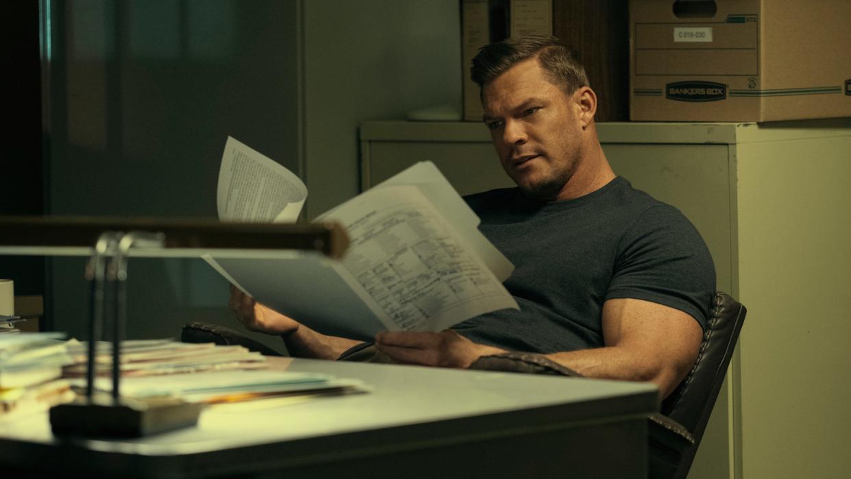  Jack Reacher (Alan Ritchson) reads a report at a desk in Reacher season 2. 