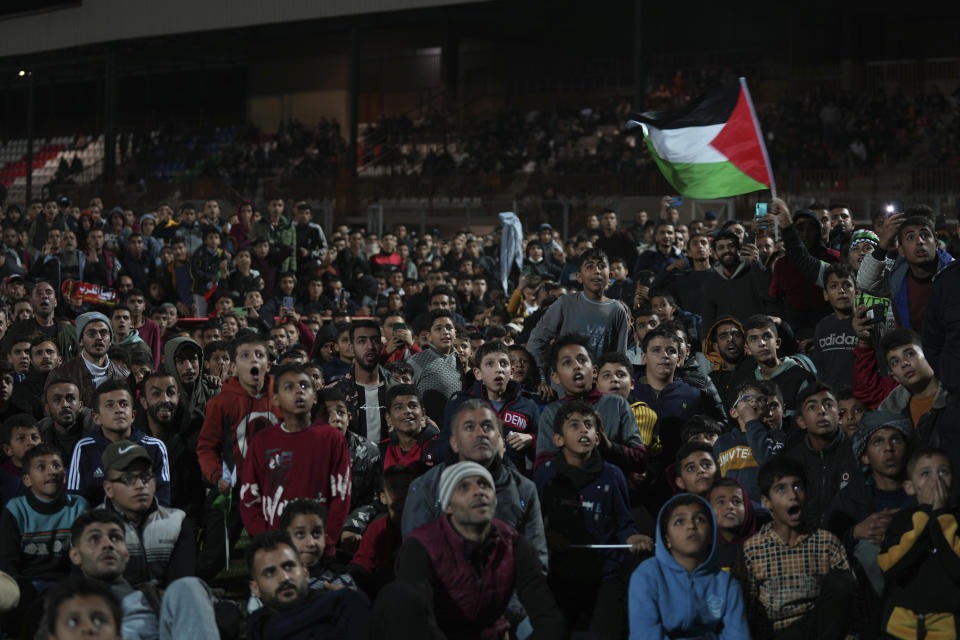 A Palestinian man waves his national flag while others watch a live broadcast of the World Cup semifinal soccer match between Morocco and France played in Qatar, at the municipality stadium in Rafah refugee camp, Southern Gaza Strip, Wednesday, Dec. 14, 2022. (AP Photo/Adel Hana)