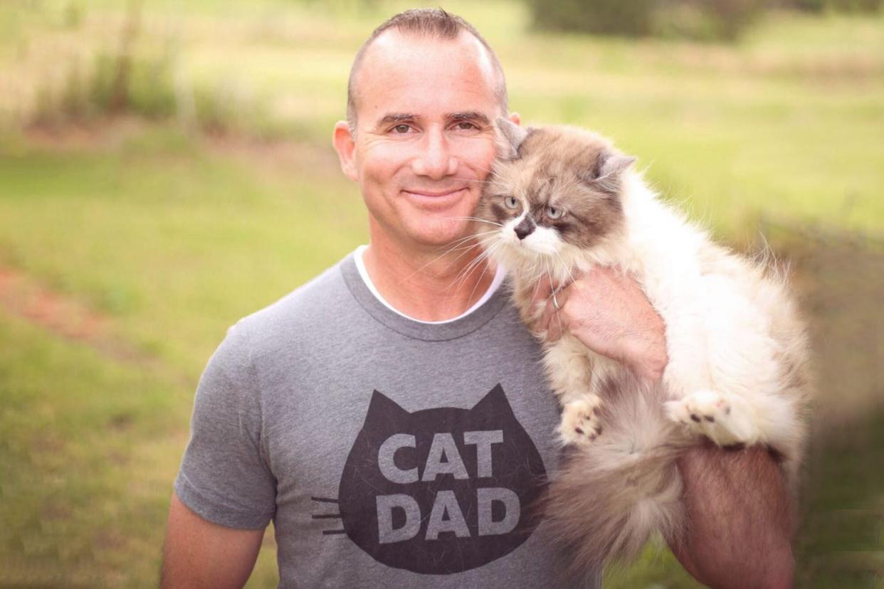 man wearing cat dad shirt holding a cat outside