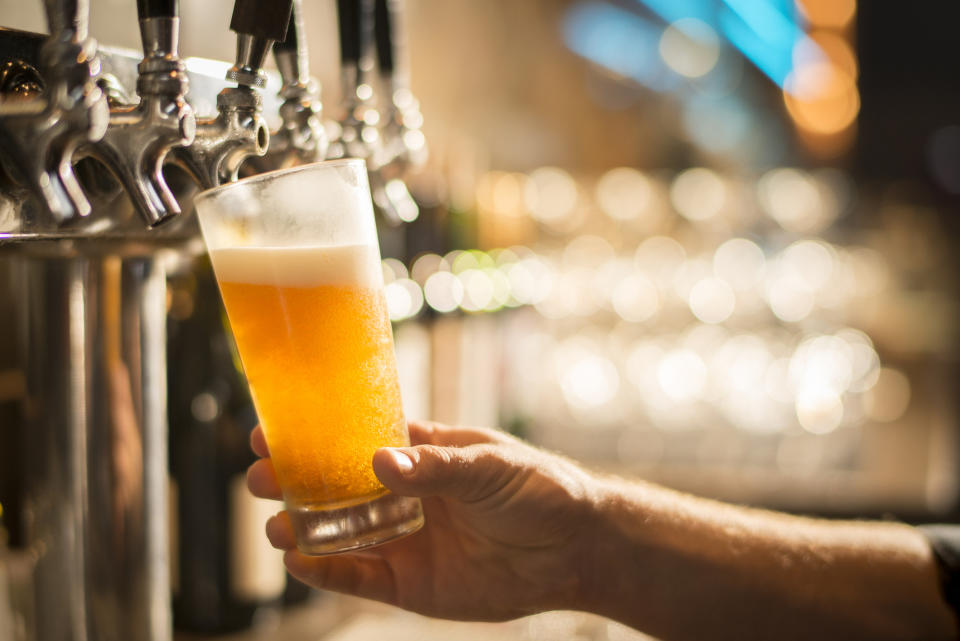 A hand holds a glass filled with beer under a tap at a bar, with the bar's taps and blurred lights in the background