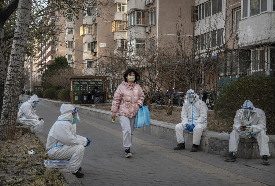BEIJING, CHINA - DECEMBER 06: A pedestrian walks by epidemic control workers who work in sanitation wearing PPE to protect against the spread of COVID-19 as they wait to remove medical waste taken from apartments where people who have tested positive are doing home quarantine on December 6, 2022 in Beijing, China.  In recent weeks, China has been recording some of its highest number of COVID-19 cases since the pandemic began, while many restrictions have been relaxed, there can still be targeted lockdowns and testing, mask mandates, and quarantines. The government has launched a vaccination drive targeting the elderly, and indicated that some positive cases are able to quarantine at home instead of at a government facility. (Photo by Kevin Frayer/Getty Images)