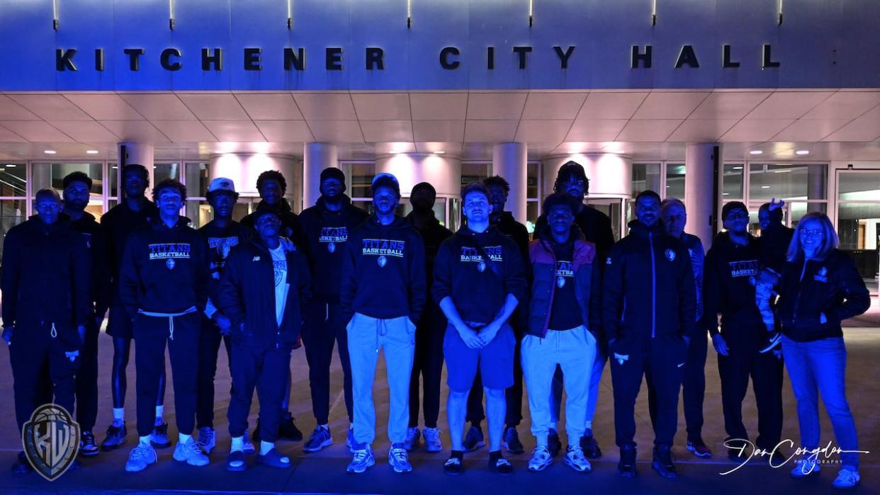 K-W Titans stand in front of Kitchener's city hall, which has been lit up blue to honour the team during the playoffs.  (Dan Congdon - image credit)