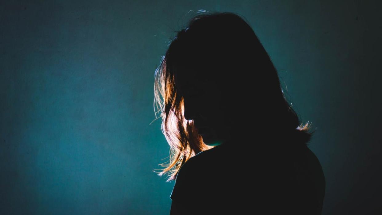 silhouette of depress woman standing in the dark with light shine behind