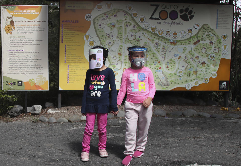 Girls wearing face shields as a preventive measure against the new coronavirus wait for their parents to enter the zoo on the outskirts of Quito, in Guayllabamba, Ecuador, Wednesday, July 8, 2020. The zoo is reopening but with strict new social distancing protocols for visitors due to the COVID-19 pandemic. (AP Photo/Dolores Ochoa)