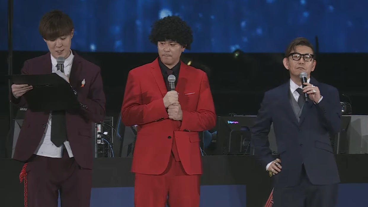  Naoki Yoshida stands on the right with his hand on his hip, wearing a blue suit.,. 