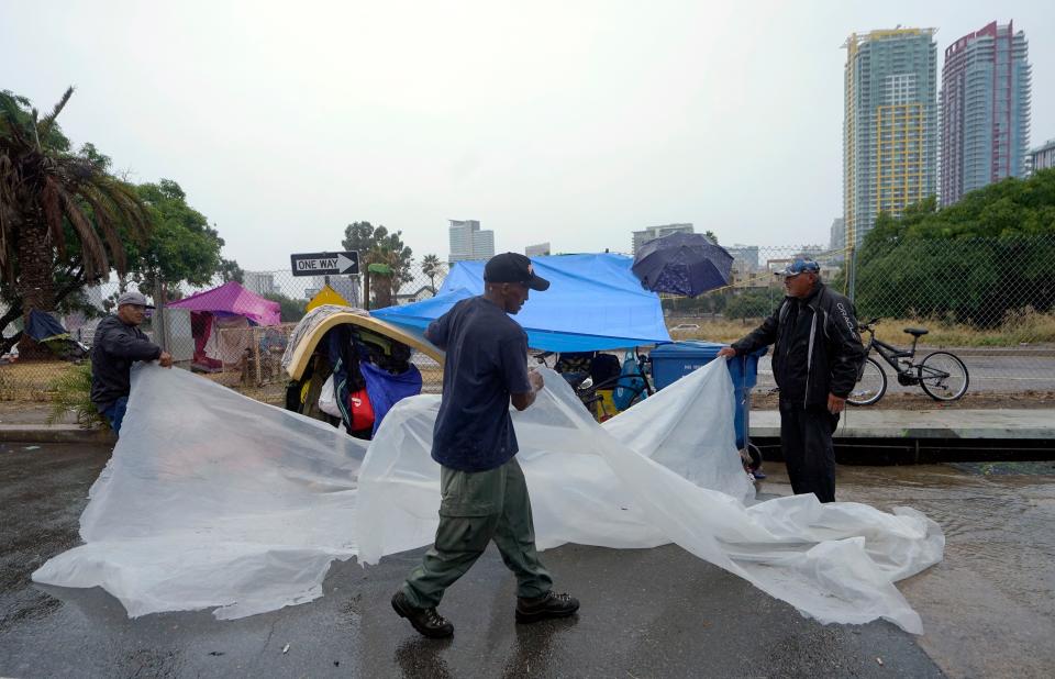 Homeless people carry a plastic tarp to shield themselves from a light rain brought by Tropical Storm Hilary in downtown San Diego, Sunday, Aug. 20, 2023. (AP Photo/Damian Dovarganes)