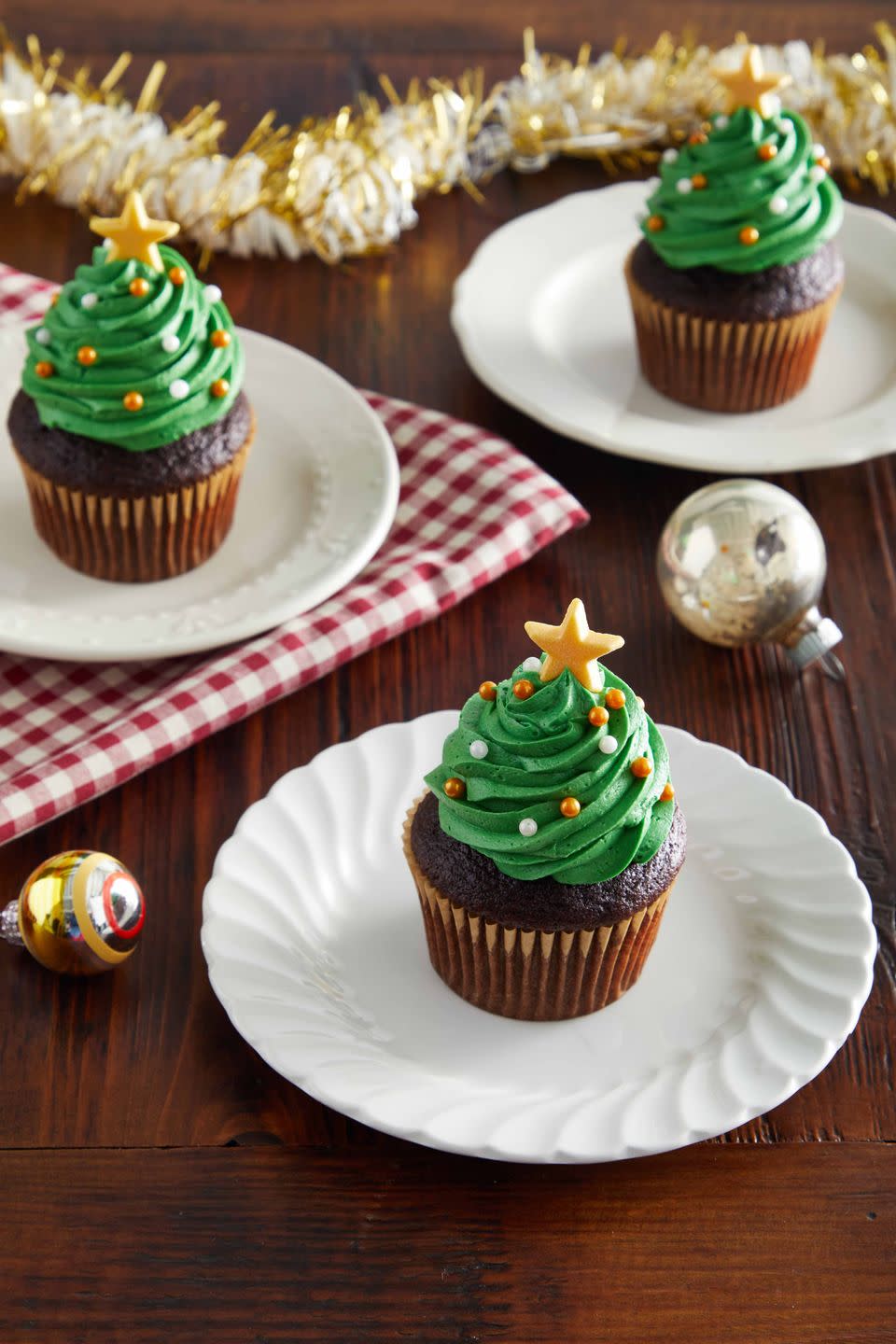 chocolate cupcakes decorated with green frosting made to look like a tree and small gold and white candy ornaments