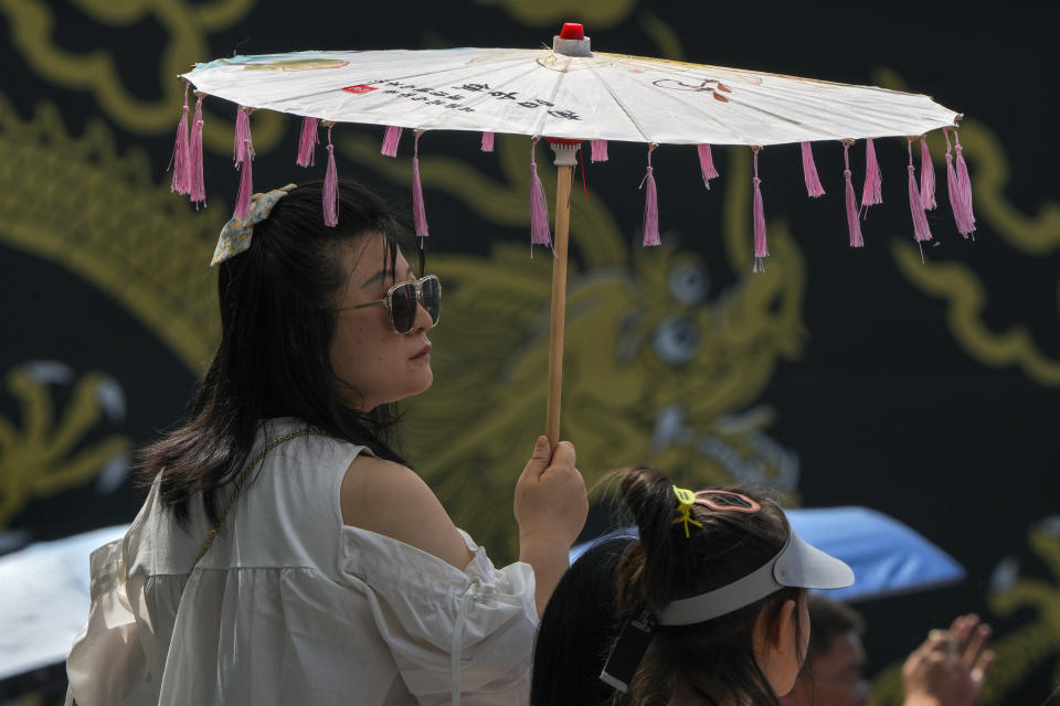 A woman carries an umbrella to shield from the sun as residents watch the Dragon Boat race during the Dragon Boat festival at a canal in Tongzhou, on the outskirts of Beijing, Monday, June 10, 2024. The Duanwu festival, also known as the Dragon Boat festival, falls on the fifth day of the fifth month of the Chinese lunar calendar and is marked by celebrations like eating rice dumplings and racing dragon boats. (AP Photo/Andy Wong)