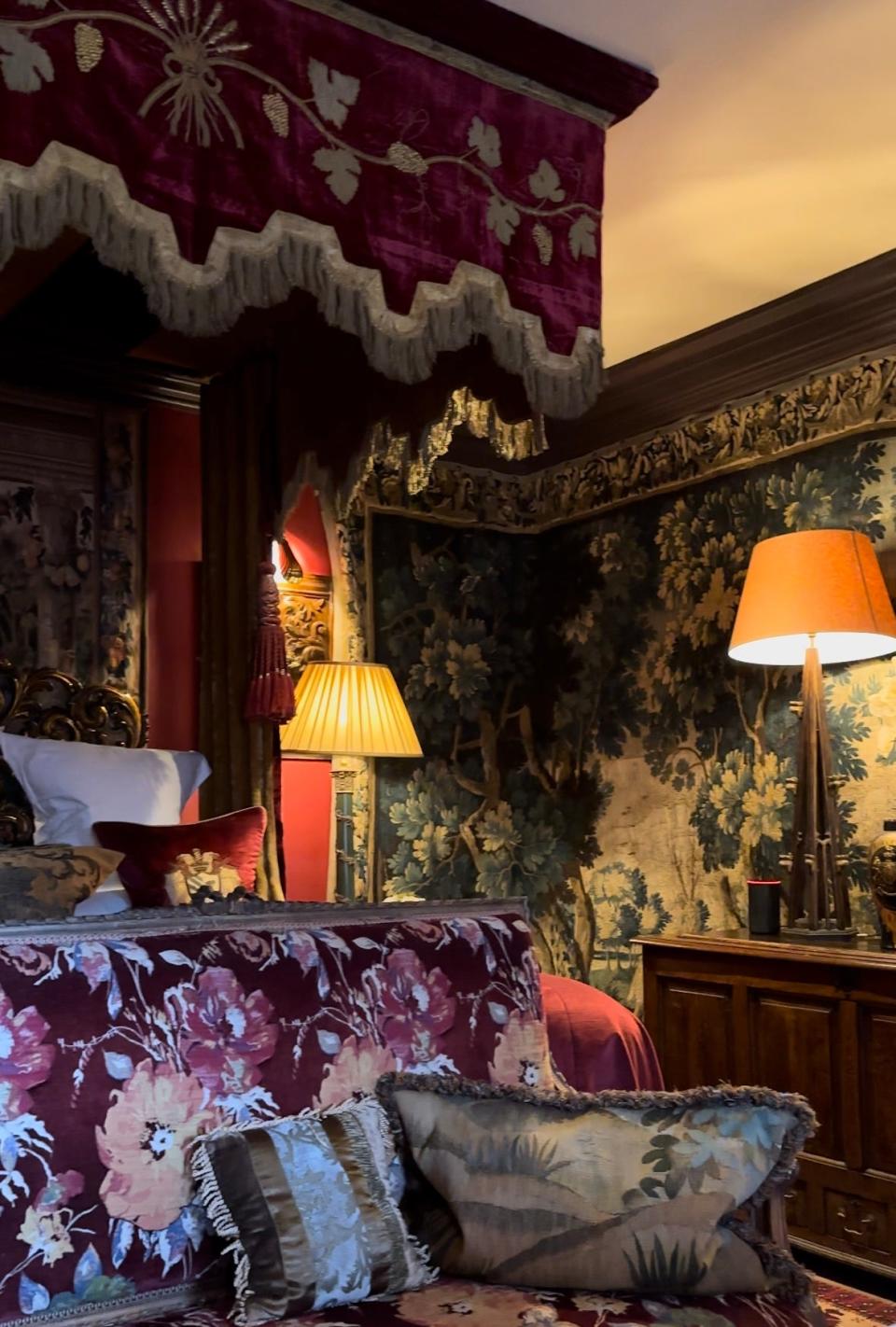 A fringe hem four poster bed in a red fabric with tapestry covering the walls