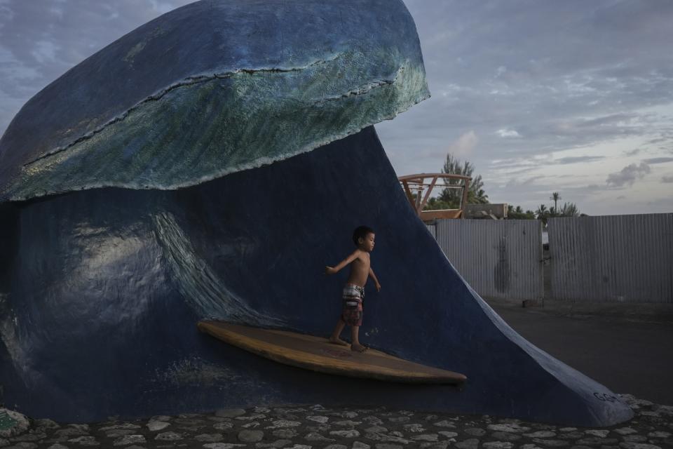 A child plays on a sculpture of the Teahupo'o wave at the end of the road, Tahiti, French Polynesia, Saturday, Jan. 13, 2024. (AP Photo/Daniel Cole)