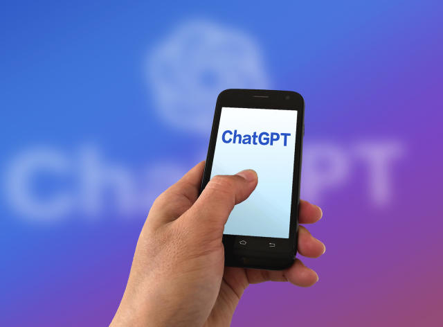 A picture of a human hand holding a phone with the words ChatGPT on it.